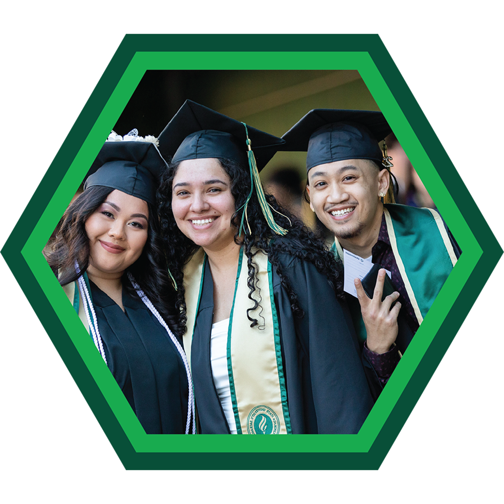 Three students with graduation gowns smiling to the camera.